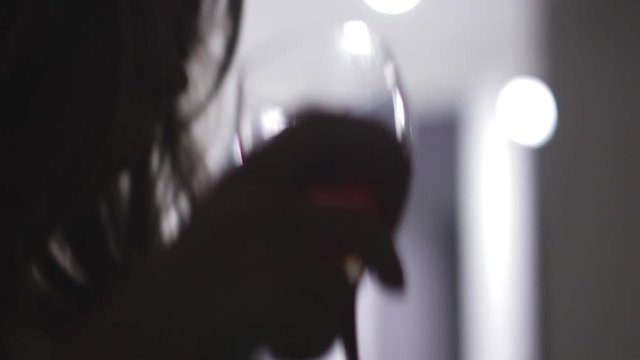 One young attractive woman drinking red wine out of glass in the dark in the apartment. Close up shot. 