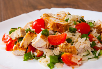 chicken and rice salad with fresh tomatoes in a plate on wooden table