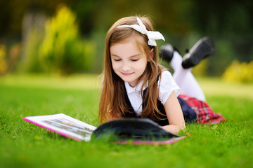 Adorable little girl laying on a grass reading a book © MNStudio