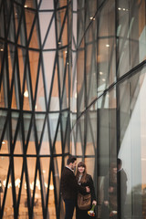 Stylish loving couple kissing and hugging near modern building