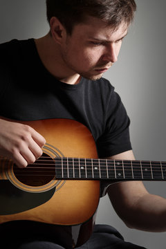 Young man with light beard playing acoustic guitar