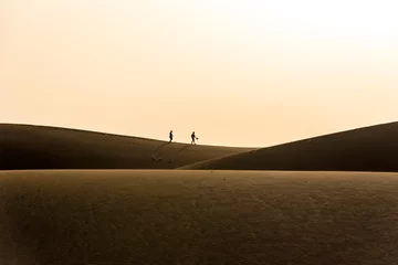 Zelfklevend Fotobehang Paar wandelen in de woestijn met zonsondergang © Simon Dannhauer