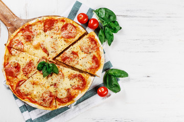 Hot true PEPPERONI ITALIAN PIZZA with salami and cheese. TOP VIEW Tasty traditional pepperoni pizza on board on white wooden table with decoration and slice. Copy space for your logo