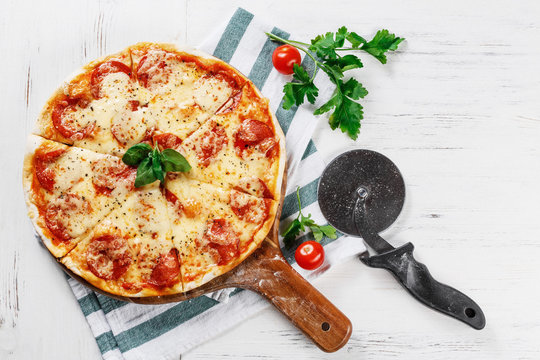 Hot true PEPPERONI ITALIAN PIZZA with salami and cheese. TOP VIEW Tasty traditional pepperoni pizza on board on white wooden table with tomato and basil. Copy space for your logo. 