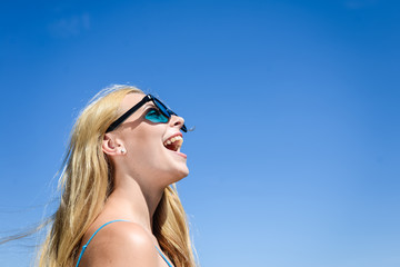 Closeup of delighted happy young blond pretty lady in sunglasses over blue sky on summer day outdoors