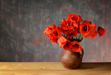 Naklejka premium Red poppies in a ceramic vase on a wooden table
