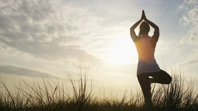 4K Silhouette of a woman doing yoga on a beach hilltop, in slow motion