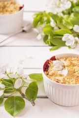 Crumble with strawberry and black currant on a white wooden background with flowering branches of apple trees 