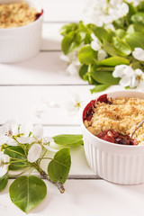 Crumble with strawberry and black currant on a white wooden background with flowering branches of apple trees 