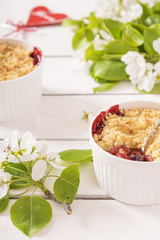 Crumble with strawberry and black currant on a white wooden background with flowering branches of apple trees 