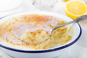 Lemon pudding cake with fresh lemons on a white wooden background.