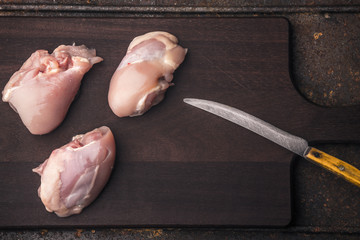 Several chicken thighs without skin and a knife on a wooden boar