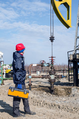 Worker near wellhead with the tool box in his hand in the oilfield. Pumpjack background. Oil and gas concept. 
