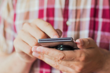 Close up hands man in plaid shirt using smart phone indoor