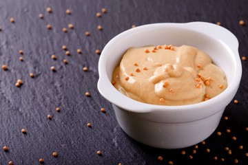 Mustard in white bowl on black slate stone