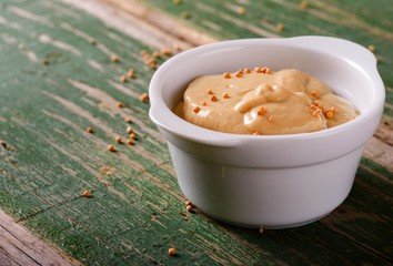 Mustard in white bowl on green wooden board