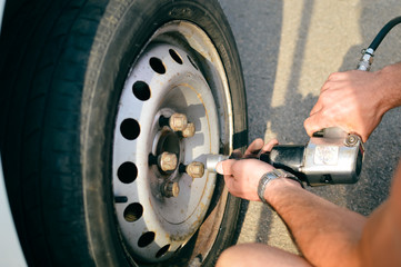 Closeup of person checking fixing bolts on vehicle tire with bare hands. 
