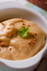 Orange mustard in white bowl with green herb