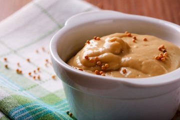 Orange mustard with seeds in white bowl