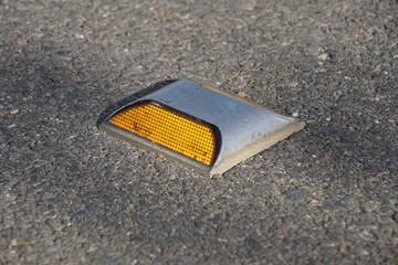 Metal road stud with yellow reflector on asphalt road
