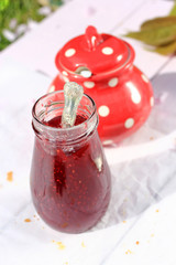A jar of fresh raspberry jam on light rustic background, close up, in the garden, selective focus