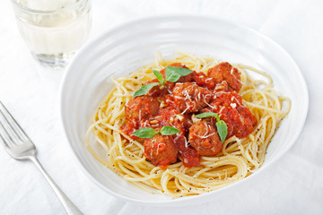 Meatballs in tomato sauce and fresh basil with spaghetti on a white plate
