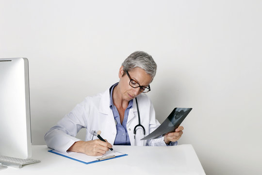 Ärztin am Schreibtisch macht Notizen anhand eines Röntgenbildes