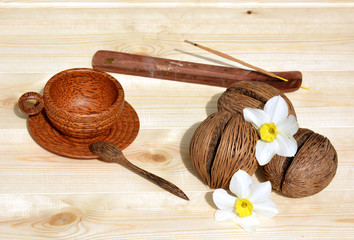 Decorative coconuts and tea utensils from wood with a narcissist and stand with the spices on a background of pine boards