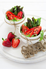 Fresh salad with strawberry, arugula, avocado and black sesame in white cups on white wooden background