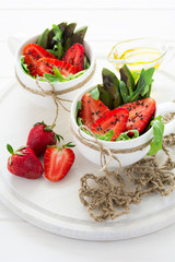 Fresh salad with strawberry, arugula, avocado and black sesame in white cups on white wooden background