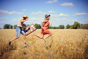Joyful young couple having fun in wheat field. Excited man and woman running with retro leather...
