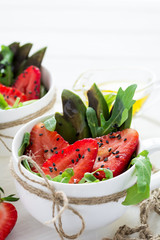 Fresh salad with strawberry, arugula, avocado and black sesame in white cups on white wooden background