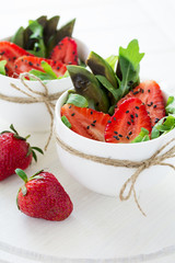 Fresh salad with strawberry, arugula, avocado and black sesame in white cups on white wooden background