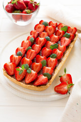 Homemade tart with strawberries and strawberry curd decorated mint leaves on white wooden background