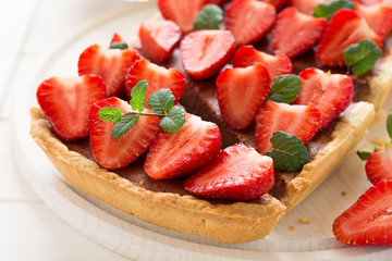 Homemade tart with strawberries and strawberry curd decorated mint leaves on white wooden background