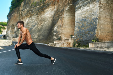Fototapeta na wymiar Fitness Exercise. Athletic Active Man With Fit Muscular Body Stretching, Exercising Before Running. Athlete Warming Up And Preparing For Workout. Male Runner Doing Stretches Outdoor. Sports Concept