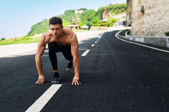 Athletics. Athletic Man With Fit Muscular Body In Starting Position For Running On Road. Handsome Runner Ready To Start Sprint Race. Fitness Model Training Outdoors In Summer. Sports Workout Concept