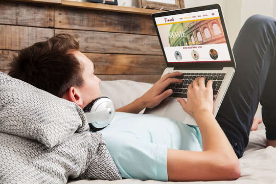 Man lying at home using a laptop to book travel destination.