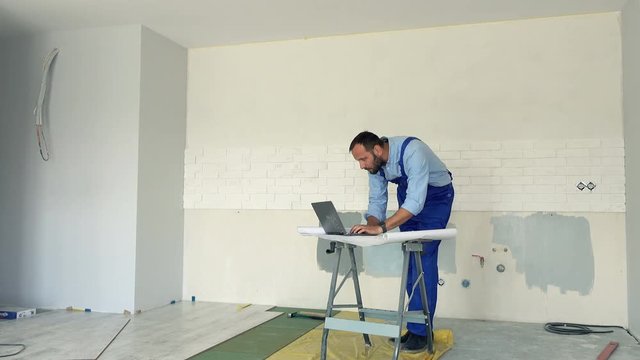 Male worker working with laptop and blueprints at new home
