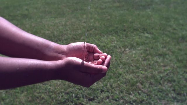 Hands of African American child catching water as it falls in slow motion.