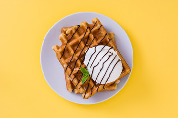 Waffles with chocolate sauce, ice cream and mint on yellow background
