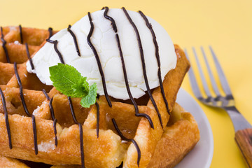 Waffles with chocolate sauce, ice cream and mint on yellow background
