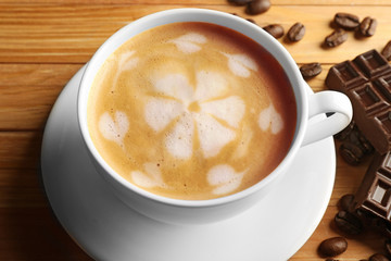 Cup of coffee latte art with grains and chocolate bar on wooden table, closeup