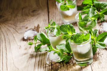 Green mint tea with ice in glasses, vintage wooden background, s
