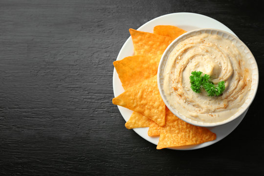 Ceramic bowl of tasty hummus with chips and parsley on table