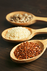 Sesame, flax and sunflower seeds in wooden spoons on table, closeup
