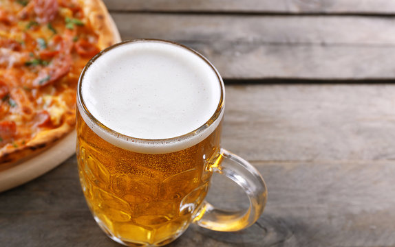 Tasty pizza and glass of beer are on wooden table, close up