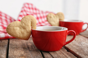 Heart shape cookie on cup of coffee on wooden table closeup