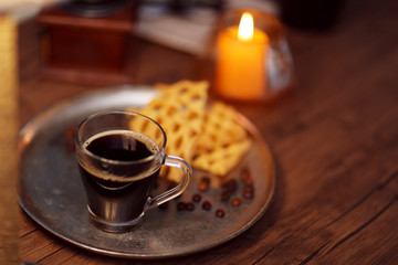 Glass cup of coffee with waffles on dark table