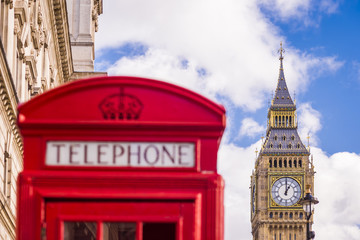 Traditional red british telephone box and Big Ben at the background with blue sky and clouds - London, UK